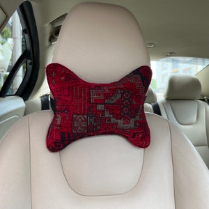May include: A red and black patterned neck pillow for car seats. The pillow is shaped like a bone and has a geometric design.