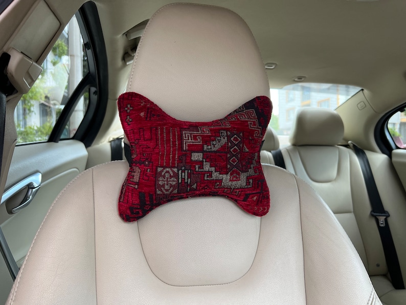 May include: A red and black patterned neck pillow for car seats. The pillow is shaped like a bone and has a geometric design.