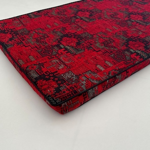Op de afbeelding: Rood en zwart gepatroneerd kussen met een zwarte bies. Het kussen heeft een geometrisch ontwerp.