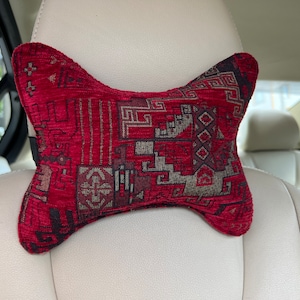 May include: A red and black patterned car headrest pillow. The pillow is shaped like a bow tie and has a geometric design.