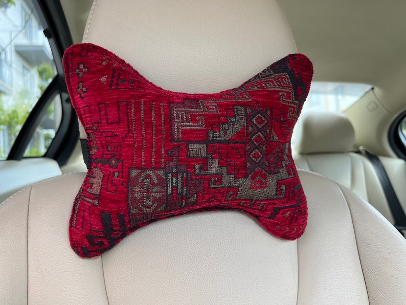 May include: A red and black patterned car headrest pillow. The pillow is shaped like a bow tie and has a geometric design.