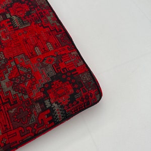 Puede incluir: Coj&iacute;n rojo y negro con estampado y borde negro. El coj&iacute;n est&aacute; hecho de una tela tejida con un dise&ntilde;o geom&eacute;trico.
