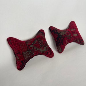 May include: Two red patterned pillows with a unique shape. The pillows are shaped like a bow tie with the ends pointed.