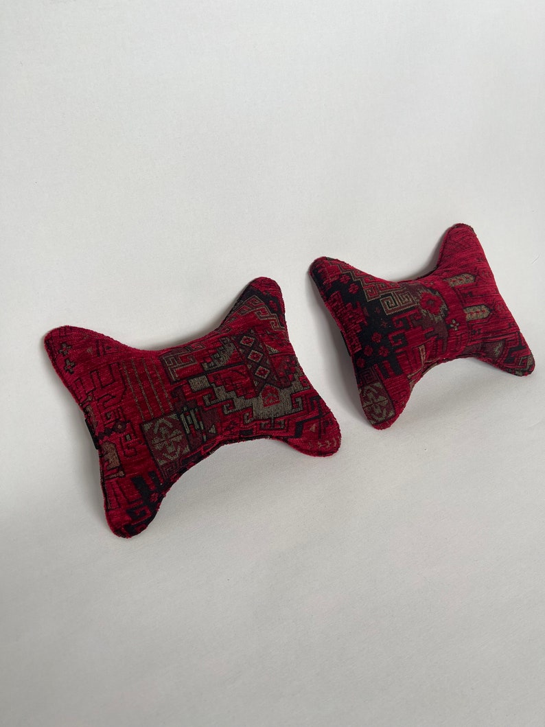 May include: Two red patterned pillows with a unique shape. The pillows are shaped like a bow tie with the ends pointed.