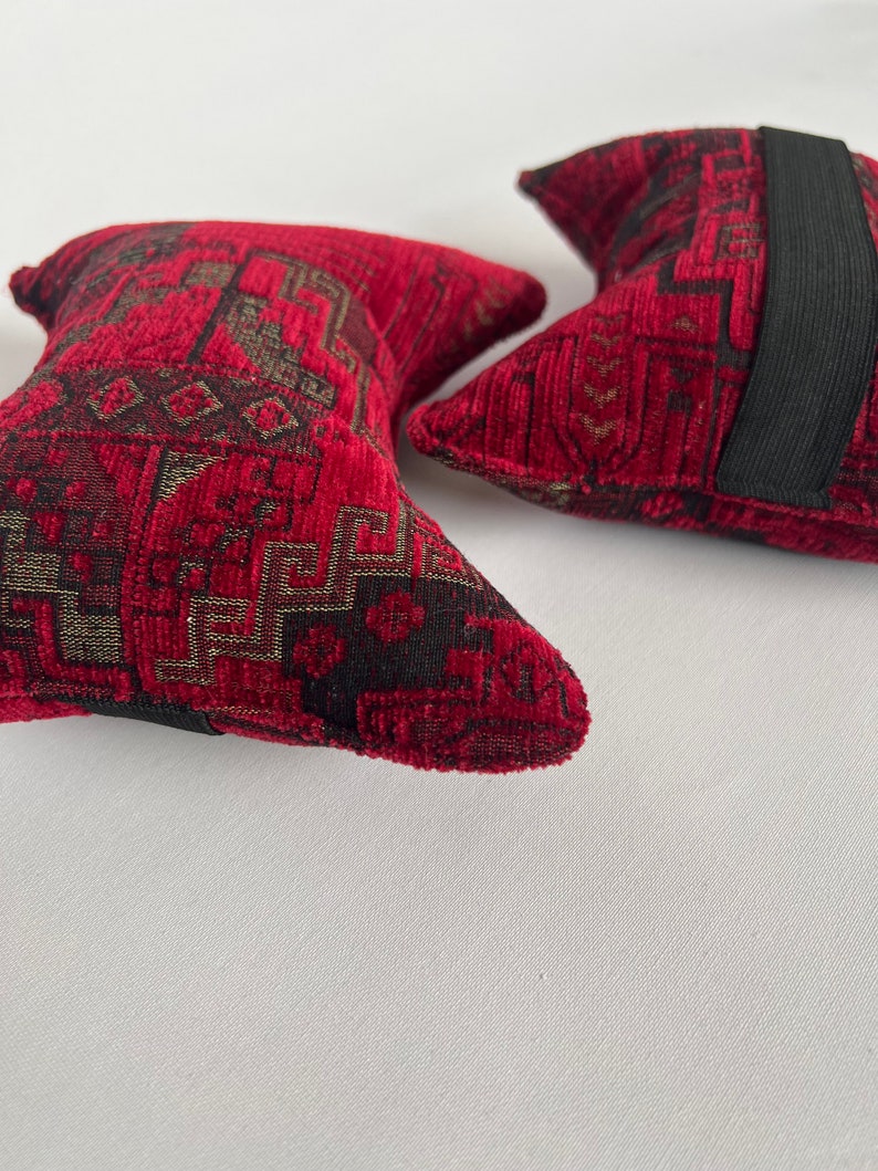 May include: Two red and black patterned throw pillows with black elastic bands. The pillows have a geometric design.