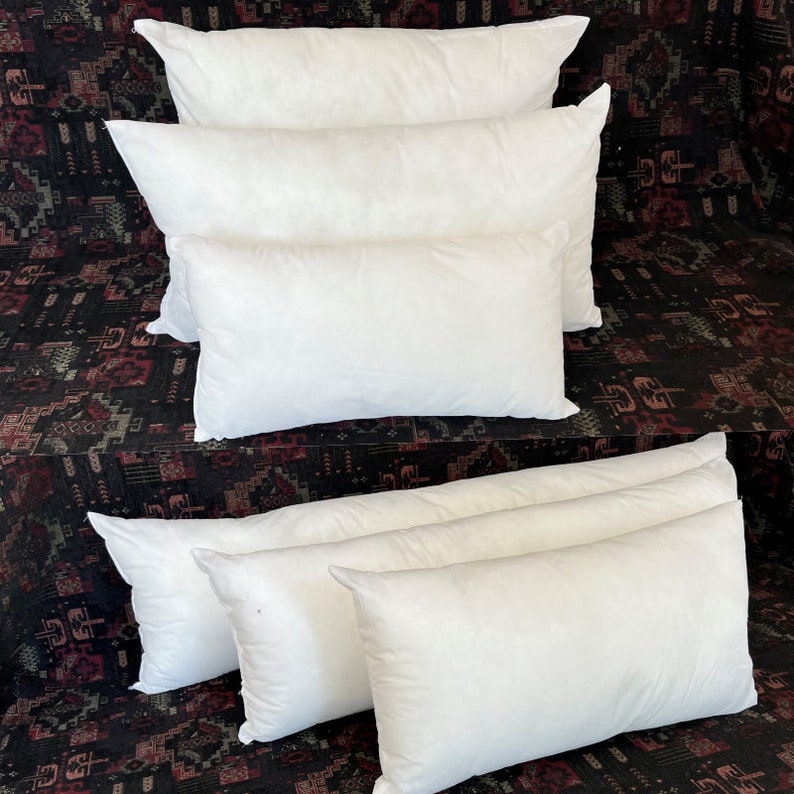 May include: A stack of five white pillow inserts. The pillows are arranged in a pyramid shape, with the largest pillow at the bottom and the smallest pillow at the top.