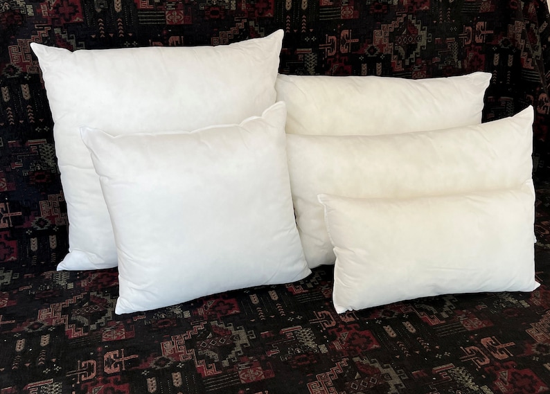 May include: Five white pillow inserts of varying sizes stacked on top of each other. The pillows are arranged in a pyramid shape with the largest pillow at the bottom and the smallest pillow at the top.