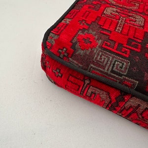 Puede incluir: Primer plano de la esquina de un coj&iacute;n rojo y negro con estampado y borde negro.