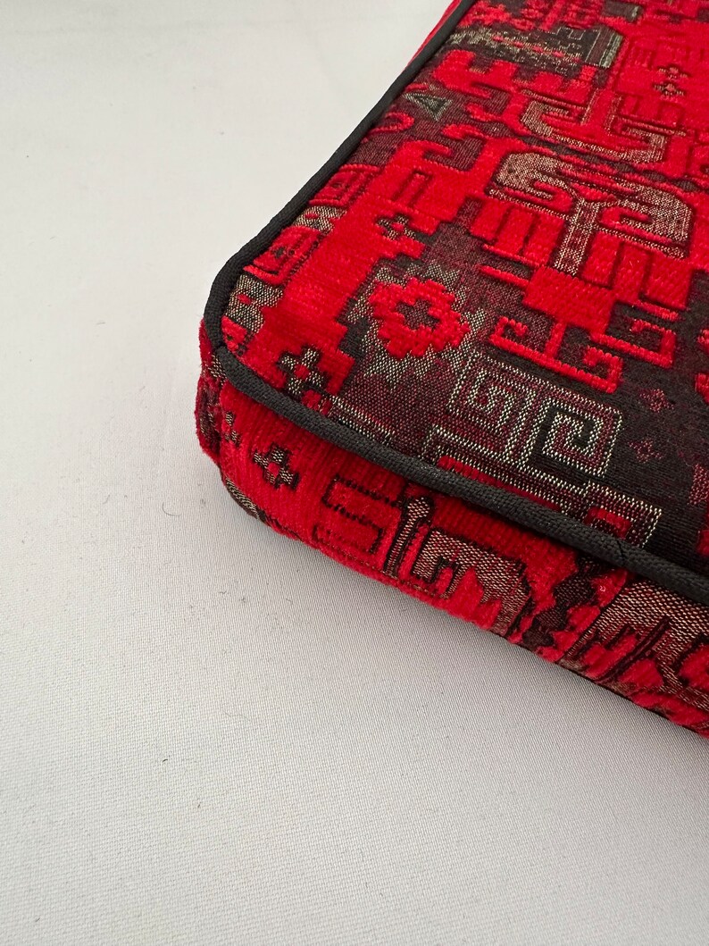 Puede incluir: Primer plano de la esquina de un coj&iacute;n rojo y negro con estampado y borde negro.