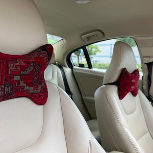 May include: Two car seats with red and brown patterned headrest pillows. The seats are beige leather.
