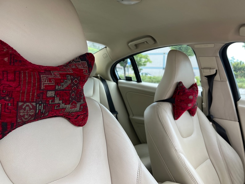 May include: Two car seats with red and brown patterned headrest pillows. The seats are beige leather.