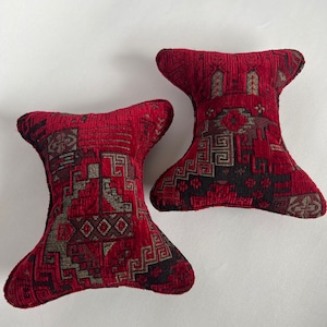May include: Two red and black patterned throw pillows with a geometric design. The pillows are shaped like a teardrop with a pointed end.