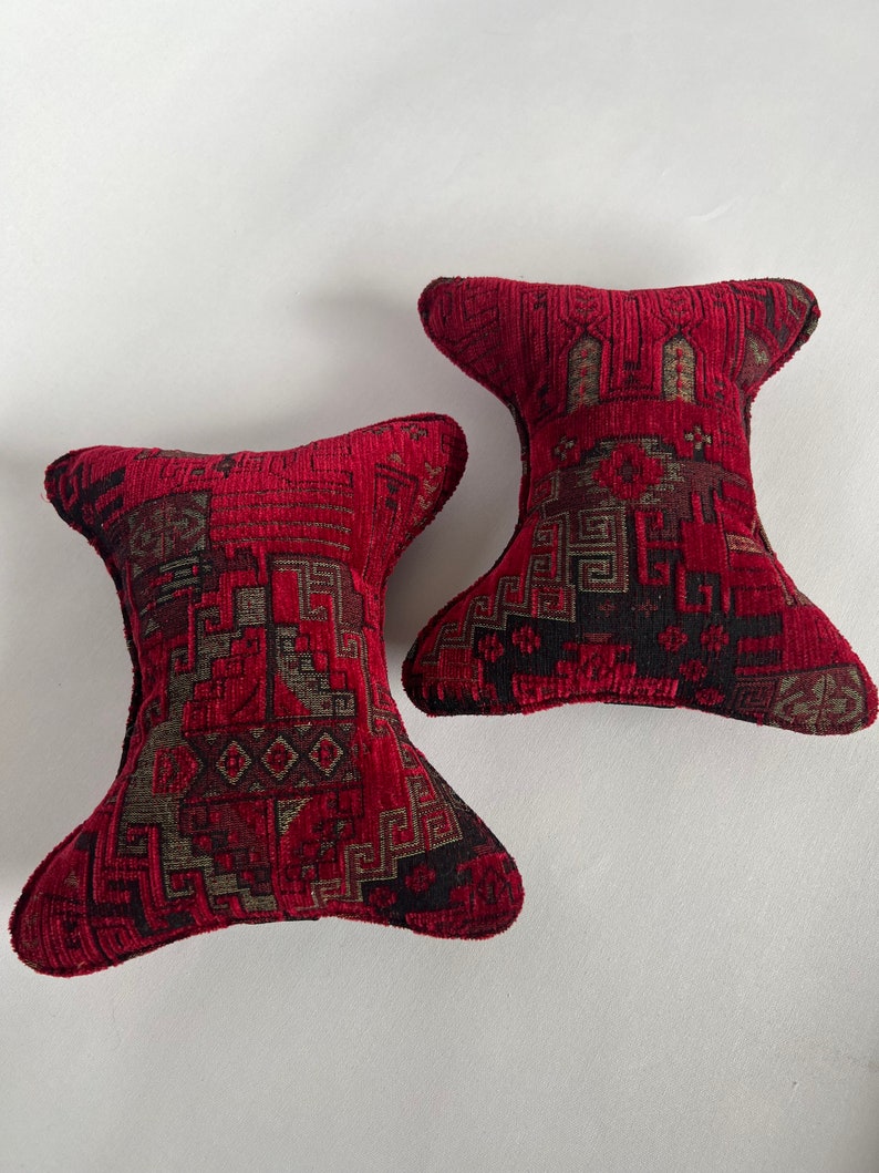 May include: Two red and black patterned throw pillows with a geometric design. The pillows are shaped like a teardrop with a pointed end.