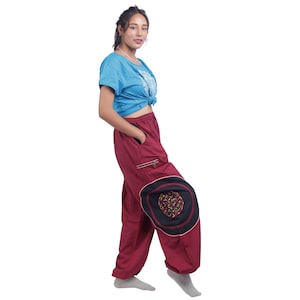 Könnte beinhalten: Eine Frau trägt ein blaues T-Shirt, das in der Taille gebunden ist, und eine weinrote Hose mit einem schwarzen und bunten Kreisdesign am linken Bein.