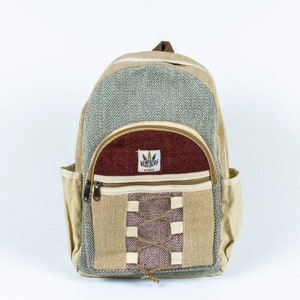 Puede incluir: Una mochila beige y granate con un patrón de espiga. La mochila tiene un bolsillo frontal con cremallera, bolsillos laterales y un asa superior. La marca "HEMPATHY" es visible en el bolsillo frontal.