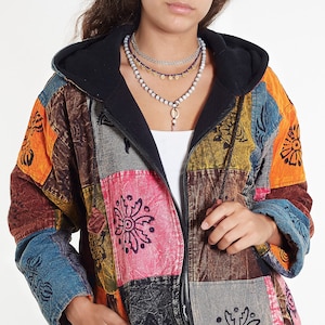 Może przedstawiać: Wielokolorowa kurtka w patchworku z kapturem podszytym czarnym polarem. Kurtka zapinana na zamek błyskawiczny i zdobiona różnymi wzorami kwiatowymi.