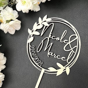 Könnte beinhalten: Weißer Kuchentopper aus Holz mit einem runden Design mit den Namen "Nicole & Marcel" und dem Datum "2023.07.2023".