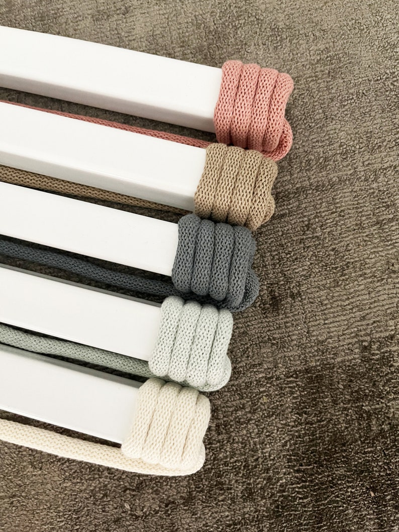 Op de afbeelding: Vijf spoelen met verschillende kleuren katoenen koord gewikkeld rond witte deuvels. De kleuren zijn roze, beige, grijs, lichtgroen en cr&egrave;me.