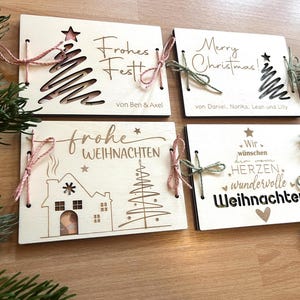 May include: Four wooden Christmas cards with festive designs. Each card features laser-cut images of a Christmas tree, house, and star, along with holiday greetings in German and English. Tied with twine and bows.