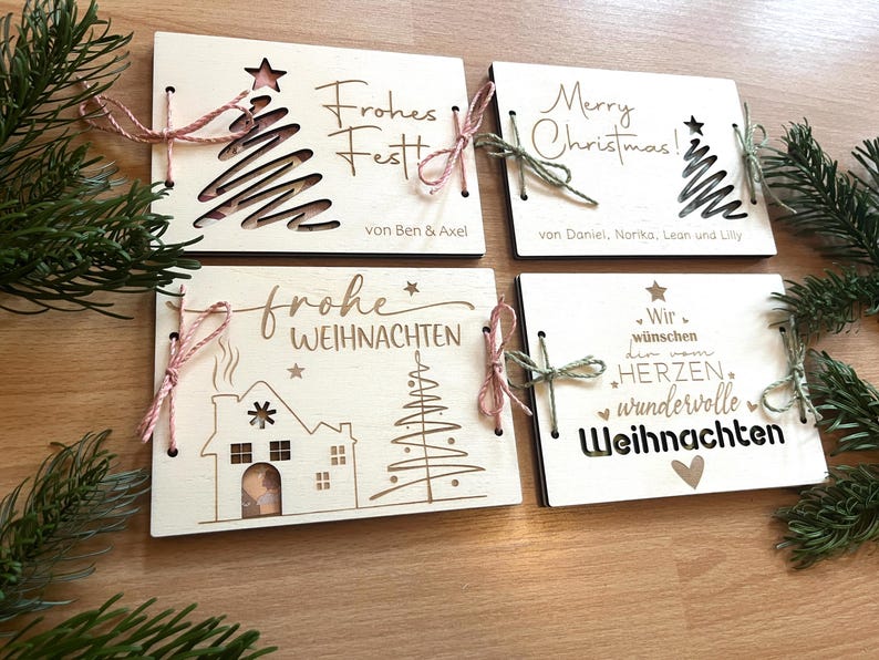 May include: Four wooden Christmas cards with festive designs. Each card features laser-cut images of a Christmas tree, house, and star, along with holiday greetings in German and English. Tied with twine and bows.