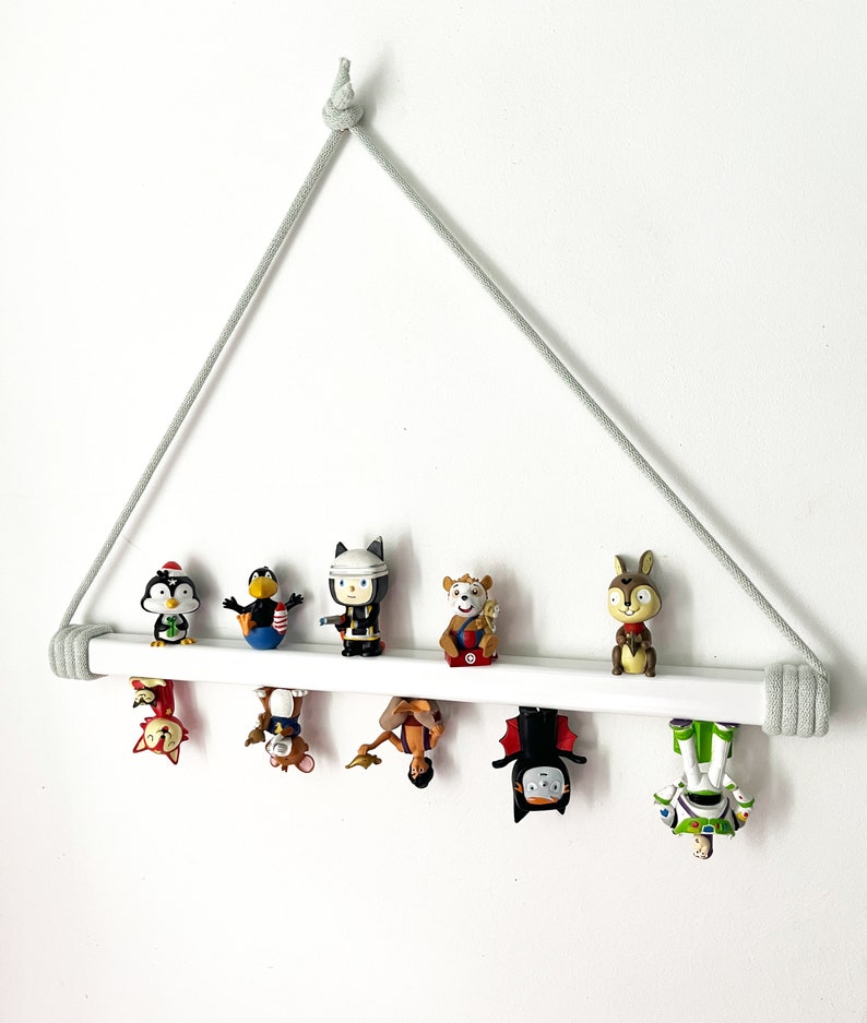 Op de afbeelding: Een wit houten plank met een grijs touw dat aan het plafond hangt. De plank heeft een verscheidenheid aan kleine speelgoedjes, waaronder een pingu&iuml;n, een vogel, een brandweerman, een beer, een konijn, een vos, een kat, een prinses, een vleermuis en een ruimte-ranger.