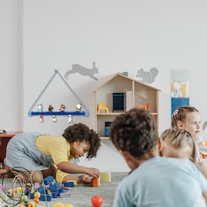 May include: A blue wooden shelf with a rope hanger is mounted on a white wall. The shelf is holding small colorful figurines. A group of children are playing with building blocks in a room with a dollhouse on the wall.
