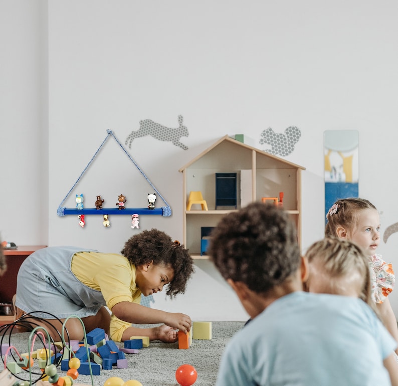 May include: A blue wooden shelf with a rope hanger is mounted on a white wall. The shelf is holding small colorful figurines. A group of children are playing with building blocks in a room with a dollhouse on the wall.