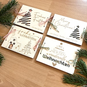 May include: Four wooden Christmas cards with laser-cut designs and text. Each card features a different festive design, including Christmas trees and holiday greetings. Tied with twine, they are arranged on a wooden surface.