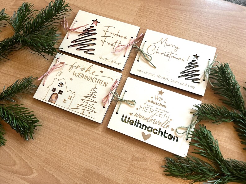 May include: Four wooden Christmas cards with laser-cut designs and text. Each card features a different festive design, including Christmas trees and holiday greetings. Tied with twine, they are arranged on a wooden surface.
