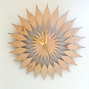 May include: A wooden wall clock with a sunflower design. The clock has gold-colored hands and a light brown wood finish.