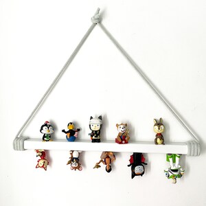 Op de afbeelding: Een wit houten plank met een grijze touwhouder, met daarop verschillende kleine beeldjes. De beeldjes zijn een pingu&iuml;n, een vogel, een robot, een hert, een figuur met een kroon, een vleermuis en een robot.