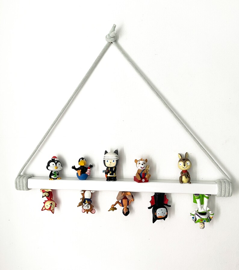 Op de afbeelding: Een wit houten plank met een grijze touwhouder, met daarop verschillende kleine beeldjes. De beeldjes zijn een pingu&iuml;n, een vogel, een robot, een hert, een figuur met een kroon, een vleermuis en een robot.