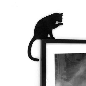 Könnte beinhalten: Schwarze Silhouette einer Katze, die auf einem schwarzen Bilderrahmen sitzt. Die Katze schaut nach rechts und hat ihre Pfote erhoben. Der Bilderrahmen ist leer.