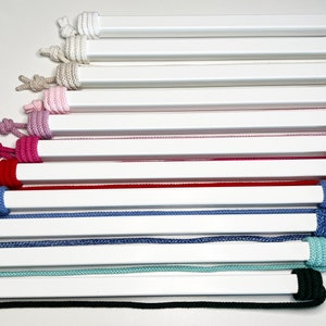 May include: A collection of 10 different coloured cords wrapped around white dowels. The cords are arranged in a fan shape, with the darkest cord at the bottom and the lightest cord at the top. The cords are all the same length and are made of a soft, textured material.