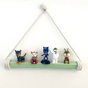 May include: A light green wooden shelf with a white rope hanging from the ceiling. The shelf is decorated with five small figurines, including a dog, a cat, a superhero, a snowman, and a rabbit.