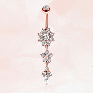 May include: A rose gold belly button ring with three dangling charms. Each charm is a flower shape with clear sparkling stones.