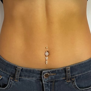 May include: A gold belly button ring with a dangling charm featuring three flower-shaped crystals.