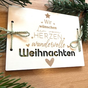 May include: A light-colored wooden Christmas card with the German text "Wir w&uuml;nschen dir vom HERZEN wundervolle Weihnachten" (We wish you a wonderful Christmas from the heart). The card is tied with green twine and decorated with a star and heart.