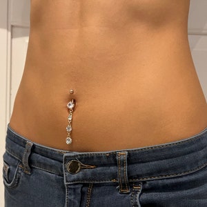 K&ouml;nnte beinhalten: Nahaufnahme des Bauches einer Person mit einem Bauchnabelpiercing, das mit einer herabh&auml;ngenden Kette aus klaren Strasssteinen verziert ist.