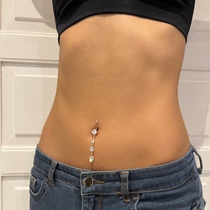 K&ouml;nnte beinhalten: Ein goldener Bauchnabelpiercing mit einer herabh&auml;ngenden Kette aus klaren Strasssteinen.