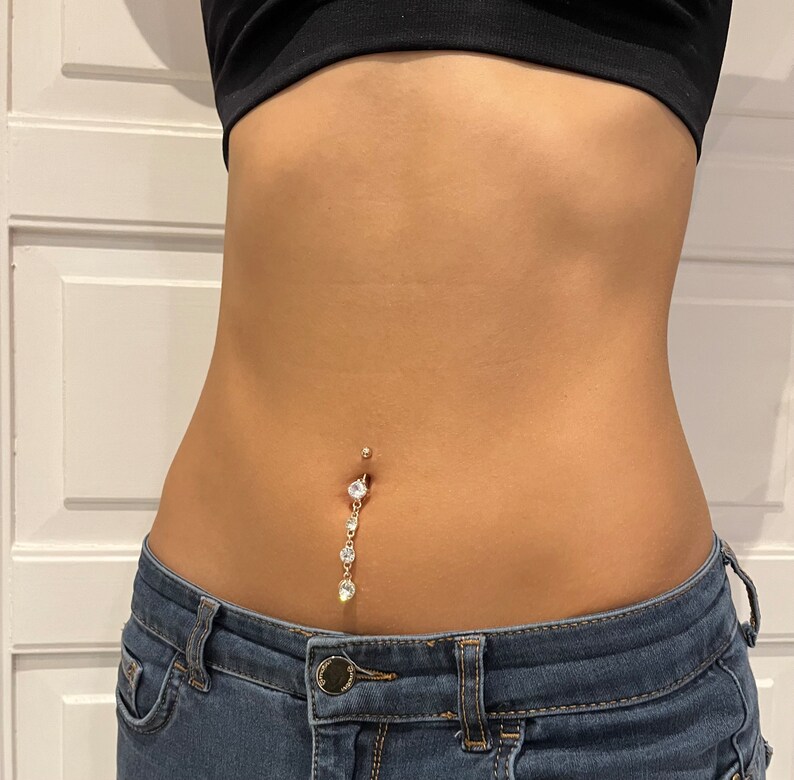 K&ouml;nnte beinhalten: Ein goldener Bauchnabelpiercing mit einer herabh&auml;ngenden Kette aus klaren Strasssteinen.
