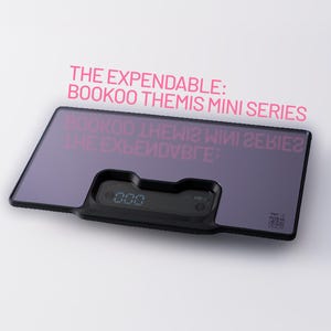 Op de afbeelding: Een zwarte en paarse digitale keukenweegschaal met de tekst "THE EXPENDABLE: BOOKOO THEMIS MINI SERIES" in roze. De weegschaal heeft een digitale display met "000".