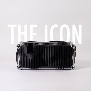 Könnte beinhalten: Ein schwarzer rechteckiger Organizer mit vertikalen Rippendetails und verchromten Eckverbindern. Die Oberseite weist mehrere kreisförmige Aussparungen und einen geformten Schlitz auf. Der Text THE ICON ist in großen weißen Buchstaben über dem Objekt zu sehen.