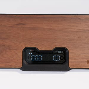 Puede incluir: Báscula de cocina rectangular de madera con pantalla digital. La báscula tiene un acabado de veta de madera oscura y una pantalla digital negra que muestra las mediciones. El nombre de la marca está impreso en la esquina inferior derecha.
