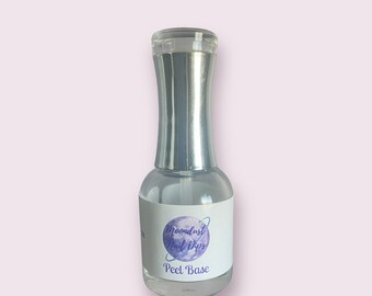 May include: A clear glass bottle of nail dip peel base with a silver cap. The bottle has a white label with the text "Moondust Nail Dips" and "Peel Base" in a purple and blue design.