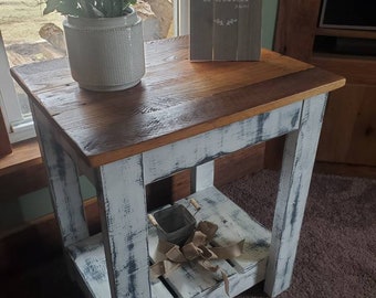 May include: A whitewashed wooden end table with a distressed finish. The table has a top shelf and a lower shelf. A small potted plant and a wooden sign with the text "do not let your heart be troubled" are on the top shelf.