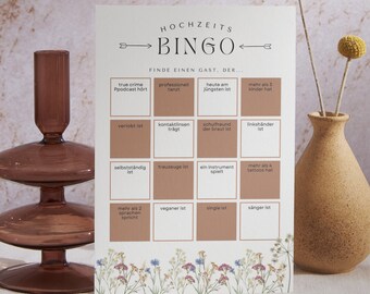 May include: A white card with brown squares and text in German. The card is titled "Hochzeits Bingo" and has a list of bingo squares with phrases like "true crime podcast hört", "professionell tanzt", "heute am jüngsten ist", "mehr als 3 kinder hat", "verlobt ist", "kontaktlinsen trägt", "schuifreund der braut ist", "linkshänder ist", "selbstständig ist", "trauzeuge ist", "ein instrument spielt", "mehr als 4 tattoos hat", "mehr als 2 sprachen spricht", "veganer ist", "single ist", and "sänger ist". The card is decorated with a floral border.