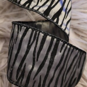 Könnte beinhalten: Schwarz-weißes Zebra-Musterband mit Satin-Finish. Das Band ist in der Mitte gefaltet und die Kanten sind vernäht.