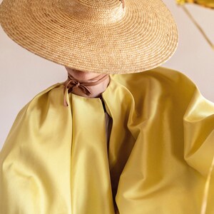 May include: A wide-brimmed straw hat with a brown ribbon tied around the crown. The hat is worn by a person wearing a yellow, flowing garment.