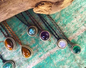 May include: A collection of gemstone necklaces with various colored stones, including tiger's eye, amethyst, moonstone, and turquoise. The necklaces are made with a simple cord and feature a silver-toned setting for each stone.